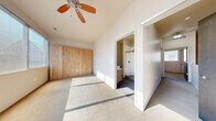 This three-story property showcases a thoughtful blend of modern design and warm natural materials throughout its multiple levels, connected by carpeted staircases with sleek dark handrails. The kitchen is a standout feature, offering white upper cabinetry contrasted by dark wood lower cabinets, light countertops, stainless steel appliances including a refrigerator, range, microwave, and dishwasher, a wood-paneled backsplash, and a large island with pendant lighting overhead. The hard wood-style flooring in the kitchen and lower-level rooms adds a contemporary feel. Upper-level rooms feature soft carpeting, vaulted ceilings with ceiling fans, and striking natural wood accent walls that lend warmth and texture to the space. Abundant natural light filters through multiple windows. A bathroom features large-format tile flooring, a vanity with modern hardware, and direct access to a walk-in closet outfitted with wire shelving for ample storage. Additional rooms feature neutral carpet, crisp white walls, and ceiling fans, providing versatile, light-filled spaces throughout this well-appointed multi-level property.