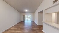 This two-bedroom, two-bathroom single-floor residence in Sunrise, Florida offers a well-organized layout designed for comfortable everyday living. The open-concept living room is a standout space, featuring soaring vaulted ceilings that amplify the sense of space, durable wood-look flooring, and a sliding glass door that leads to a private balcony with lush outdoor views. A pass-through window connects the living area to the kitchen, which is equipped with white cabinetry, a refrigerator, and a range, creating an efficient and functional cooking space with an adjacent pantry closet. The spacious primary bedroom features soft carpeting, a textured ceiling, and access to a generous walk-in closet outfitted with wire shelving for ample storage. The second bedroom is similarly carpeted and well-proportioned, with a door connecting to the hallway. Both bathrooms are clean and functional, with one featuring a full tub-shower combo, white tile surround, and terracotta tile flooring alongside a vanity with counter space. Throughout, the residence maintains a bright, neutral palette with white walls and trim that enhance the natural light flowing through the space. A dedicated hallway connects all rooms, contributing to a logical and comfortable floor plan.
