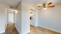 This single-floor unit offers a clean, functional layout with consistent wood-look flooring running throughout every room, creating a cohesive and easy-to-maintain aesthetic. The living area greets you at the entry, featuring a ceiling fan with light fixture, textured ceilings, and vertical blinds flanking the front door that allow for natural light and outdoor views. The galley-style kitchen is efficiently designed with white shaker cabinetry, granite-style countertops, a stainless steel sink, and a full suite of black appliances including a refrigerator, range, microwave, and dishwasher. A raised tray ceiling detail adds an architectural touch to the kitchen space. A central hallway, equipped with a thermostat, connects the private areas of the unit, including closets and additional rooms. The bedrooms are well-proportioned with neutral walls, wood-look flooring, and windows fitted with vertical blinds that bring in natural light. The bathroom features white cabinetry with brushed nickel hardware, a granite-style vanity countertop with an undermount sink, and a separate tub and shower area with clean white tile surround. The overall ambiance is bright, neutral, and move-in ready.