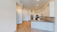 Located at 6755 W Arby Ave in Las Vegas, NV, this well-designed one-bedroom unit offers a thoughtful layout that maximizes its compact footprint. The open-concept living and kitchen area serves as the heart of the unit, featuring light hardwood-style flooring that flows seamlessly throughout the space. The kitchen is appointed with white shaker-style cabinetry extending to the ceiling with glass-front upper panels, a subway tile backsplash, dark quartz countertops, and a full suite of stainless steel appliances including a French door refrigerator, gas range, microwave, and dishwasher. A peninsula with matching countertop provides additional workspace and casual seating. Recessed lighting illuminates the kitchen and living areas. The bedroom is a comfortable retreat with soaring ceilings, a ceiling fan, and a large sliding glass door that opens to a private balcony, filling the room with natural light. The bedroom also provides direct access to the bathroom, which features warm cabinetry and a vanity mirror. Clean white walls, high ceilings, and consistent flooring throughout give the unit a bright, modern, and cohesive aesthetic.