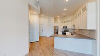 Located at 6755 W Arby Ave in Las Vegas, NV, this well-designed one-bedroom unit offers a thoughtful layout that maximizes its compact footprint. The open-concept living and kitchen area serves as the heart of the unit, featuring light hardwood-style flooring that flows seamlessly throughout the space. The kitchen is appointed with white shaker-style cabinetry extending to the ceiling with glass-front upper panels, a subway tile backsplash, dark quartz countertops, and a full suite of stainless steel appliances including a French door refrigerator, gas range, microwave, and dishwasher. A peninsula with matching countertop provides additional workspace and casual seating. Recessed lighting illuminates the kitchen and living areas. The bedroom is a comfortable retreat with soaring ceilings, a ceiling fan, and a large sliding glass door that opens to a private balcony, filling the room with natural light. The bedroom also provides direct access to the bathroom, which features warm cabinetry and a vanity mirror. Clean white walls, high ceilings, and consistent flooring throughout give the unit a bright, modern, and cohesive aesthetic.