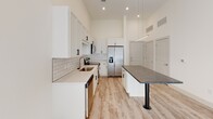 Located at 371 Technology Center Way in Rock Hill, SC, this single-floor unit offers a thoughtfully designed, modern interior with high-end finishes throughout. The open-concept living and kitchen area is anchored by impressively tall ceilings that enhance the sense of space and airiness. Light wood-look flooring runs consistently throughout, complementing the bright, neutral color palette.

The kitchen is a standout feature, outfitted with crisp white shaker-style cabinetry accented by matte black hardware, a classic white subway tile backsplash, and dark granite countertops. A generous island with a dramatic pendant light above serves as both a functional workspace and a casual gathering point. Stainless steel appliances, including a French door refrigerator, electric range, and over-the-range microwave, complete the well-equipped space. Recessed lighting and soaring ceiling height make the kitchen feel especially open and functional.

The living area extends naturally from the kitchen, bathed in natural light from French doors that lead to the exterior. A ceiling fan adds comfort to the airy room.

The bathroom is finished with the same attention to detail, featuring white cabinetry with dark countertops, a backlit vanity mirror, wood-look flooring, and a tiled walk-in shower. An adjoining walk-in closet with built-in shelving provides ample storage.