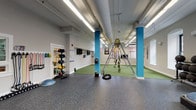 Located at 2 Clocktower in Nashua, NH, this fitness center occupies a single-floor space with a distinctive industrial character. The facility is divided into several clearly defined workout zones, each designed to support a range of exercise disciplines.

The strength training area features durable rubber flooring and an extensive selection of weight machines, free weights, barbells, dumbbells, and benches. Floor-to-ceiling mirrors line the walls, creating a spacious feel and allowing users to monitor their form. Wall-mounted televisions add an entertainment element to the workout experience. Teal-painted exposed ductwork runs along the ceilings, giving the space a modern industrial aesthetic.

The cardio zone offers multiple treadmills, elliptical trainers, and stair climbers set against a backdrop of original exposed brick walls and natural light from traditional multi-pane windows. A separate cycling area houses a row of stationary bikes on carpeted flooring, framed by salmon-colored structural columns with teal accents.

A dedicated free weights room provides a focused environment with mirrored walls, ballet-style bars, and additional dumbbell racks. The facility's entry area features teal-trimmed glass doors and windows, providing a clean transition into the workout spaces. Throughout, the combination of brick, teal, and salmon tones gives the gym a vibrant and energetic ambiance.
