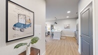 Located at 91 Kaiman Ln in Valley Park, Missouri, this single-floor residence offers a thoughtfully designed open-concept layout that seamlessly connects the kitchen, dining, and living areas. Light-toned hardwood-style flooring flows throughout, complementing the neutral gray and white color palette that lends the space a clean, modern aesthetic.

The kitchen is well-appointed with white shaker-style cabinetry, white quartz countertops, a classic subway tile backsplash, and a full suite of stainless steel appliances including a range, microwave, and refrigerator. A central island with pendant lighting provides additional prep space and casual seating, while recessed lighting ensures the entire open area is well-lit.

The living room offers a welcoming atmosphere with recessed lighting and a sliding glass door that fills the space with natural light and provides direct views of the surrounding landscape and hillside scenery. The dining area is conveniently positioned near a hallway leading to multiple rooms, each accessed through distinctive two-panel gray doors.

The entry corridor is accented with decorative touches and provides a smooth transition into the main living areas. The layout, as revealed in the dollhouse view, includes dedicated bedroom and bathroom spaces arranged for comfort and privacy, making this a well-balanced and functional single-level residence.