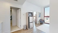 Located at 229 Duffield St in Downtown Brooklyn, this thoughtfully designed one-bedroom, one-bathroom residence makes efficient use of its compact footprint across a single floor. The layout encompasses a living room, kitchen, bedroom, bathroom, hallway, and closet — each space carefully arranged to maximize functionality.

The living area is anchored by a dramatic floor-to-ceiling window with warm wood framing, flooding the room with natural light and offering elevated views of the Brooklyn and Manhattan skyline. Light hardwood flooring runs throughout, lending a cohesive, airy feel. The kitchen is efficiently integrated into the main living space, featuring a compact refrigerator and microwave unit housed in a sleek wood-tone shelving unit.

The bedroom continues the bright, modern aesthetic with white walls, hardwood floors, and a tall window that frames urban views. High ceilings add a sense of openness beyond what the footprint might suggest.

The bathroom is finished in a contemporary style with large-format tile flooring, a wood-accented floating vanity with open shelving, an oversized mirror with overhead lighting, and a walk-in shower. Clean lines and neutral tones give the space a polished, hotel-like quality. Overall, the residence offers a streamlined, modern urban living experience in the heart of Downtown Brooklyn.