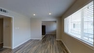 This single-floor, 2-bedroom, 2-bathroom residence offers a clean, modern aesthetic with thoughtful design choices throughout. The living area features rich, dark hardwood-style flooring that adds warmth and character to the space, complemented by crisp white ceilings with recessed lighting that provides bright, even illumination. Neutral-toned walls create a versatile backdrop, making the space easy to personalize.

The open layout connects the main living area seamlessly to the kitchen, which is visible through an open passageway and is equipped with a full-size refrigerator. Natural light flows into the living area through a window fitted with horizontal blinds, enhancing the airy and welcoming atmosphere.

The two bedrooms offer comfortable personal spaces, while the two full bathrooms provide added convenience for residents or guests. Clean white baseboards frame each room, adding a polished finishing touch throughout.

Overall, this residence strikes a balance between functionality and modern style. The consistent flooring, neutral color palette, and efficient use of space make it a practical and attractive single-floor home suitable for a variety of lifestyles.
