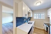 Located at 3009 W 13 Mile Rd in Royal Oak, Michigan, this 2-bedroom, 1-bathroom residence offers a thoughtfully updated interior across a single floor. The galley-style kitchen is a standout highlight, featuring crisp white shaker cabinetry with matte black hardware, striking quartz countertops with subtle veining, a deep stainless steel sink with a matte black faucet, and a bold navy blue arabesque tile backsplash. Stainless steel appliances, including a refrigerator and range, complete the modern aesthetic. Natural light filters in through a window overlooking the surrounding neighborhood. The open living and dining areas are finished with light-toned wood-look flooring, giving the shared spaces a bright, cohesive feel. A structural column adds a subtle architectural element to the layout. Both bedrooms are carpeted for comfort, with the primary bedroom featuring a sliding glass door that invites natural light and outdoor views. The updated bathroom is elegantly appointed with a white vanity, quartz countertop, round mirror with black trim, and floor-to-ceiling marble-look tile in the shower surround. Wood-look flooring ties the bathroom together with the rest of the home. Four closets provide generous storage throughout. Baseboard heating and wall-unit air conditioning serve the home's climate needs.