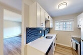Located at 3009 W 13 Mile Rd in Royal Oak, Michigan, this 2-bedroom, 1-bathroom residence offers a thoughtfully updated interior across a single floor. The galley-style kitchen is a standout highlight, featuring crisp white shaker cabinetry with matte black hardware, striking quartz countertops with subtle veining, a deep stainless steel sink with a matte black faucet, and a bold navy blue arabesque tile backsplash. Stainless steel appliances, including a refrigerator and range, complete the modern aesthetic. Natural light filters in through a window overlooking the surrounding neighborhood. The open living and dining areas are finished with light-toned wood-look flooring, giving the shared spaces a bright, cohesive feel. A structural column adds a subtle architectural element to the layout. Both bedrooms are carpeted for comfort, with the primary bedroom featuring a sliding glass door that invites natural light and outdoor views. The updated bathroom is elegantly appointed with a white vanity, quartz countertop, round mirror with black trim, and floor-to-ceiling marble-look tile in the shower surround. Wood-look flooring ties the bathroom together with the rest of the home. Four closets provide generous storage throughout. Baseboard heating and wall-unit air conditioning serve the home's climate needs.