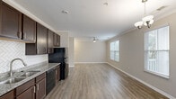 Located at 1680 Bluewater Way in Charleston, SC, this single-story, 4-bedroom, 2-bathroom home offers a well-designed floor plan that balances comfort and functionality. The open-concept kitchen and living area serves as the heart of the home, featuring rich dark-brown cabinetry, granite countertops, a herringbone-patterned tile backsplash, and black Whirlpool appliances including an electric range, built-in microwave, dishwasher, and refrigerator. The living area flows seamlessly from the kitchen, highlighted by crown molding, a ceiling fan, and natural light streaming through window blinds. Wood-look luxury vinyl plank flooring runs throughout the main living spaces, while the bedrooms are finished with plush carpeting. Bedroom windows provide views of the surrounding neighborhood greenery. The two bathrooms are appointed with granite-topped dark vanities and tiled tub-shower combinations with neutral tile flooring. A dedicated laundry room houses a full-size washer and dryer with overhead wire shelving for added storage. Two closets and two hallways contribute to the home's practical layout. Crown molding and consistent neutral tones throughout lend a cohesive, clean aesthetic to the entire residence.