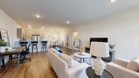 This thoughtfully designed single-floor residence offers a seamless open-concept layout that connects the living, dining, and kitchen areas into one cohesive and functional space. The living room is bright and welcoming, anchored by warm wood-look flooring, recessed lighting, and a front entry door framed by transom and arched windows that invite natural light deep into the interior.

The kitchen is outfitted with light wood cabinetry, clean white quartz countertops, and a full suite of stainless steel appliances, including a refrigerator, range, and over-the-range microwave. A peninsula with bar seating extends the kitchen's functionality and connects it naturally to the dining area, which is accented by a chandelier overhead and neutral wall tones.

A dedicated dining nook provides an intimate space for everyday meals, while the living area flows comfortably toward the main entrance, creating an easy and intuitive circulation path. The bedroom is a calm retreat, featuring plush carpet-ready flooring, neutral tones, and a generously sized window that frames views of the surrounding neighborhood.

The bathroom is clean and modern, featuring a wood-toned vanity with an undermount sink, white quartz countertop, and a shower/tub combination. The in-unit laundry room includes a full-size front-loading washer and dryer alongside a utility sink, adding considerable convenience to daily living.