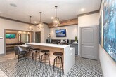 Located at 125 Jennings Mill Pkwy in Athens, Georgia, this single-floor community clubhouse offers a thoughtfully designed gathering space that blends modern aesthetics with warm, natural materials. Light wood-plank flooring and wood-paneled accent walls establish a cohesive, inviting character throughout the open-plan interior.

The central social area serves as the heart of the space, anchored by a substantial round dining table with upholstered chairs and illuminated by elegant gold pendant lights hanging above a bar counter with dark wood detailing and industrial-style barstools. A mounted flat-screen TV above the bar adds a multimedia focal point, while a geometric-patterned area rug defines the lounge zone.

Adjacent to the main gathering area, a comfortable living lounge features a plush sofa, vibrant accent chairs, and a striking natural wood accent wall. Large windows allow generous natural light to fill the room, highlighting the curated wall art and layered textiles that add personality and warmth.

Throughout the space, bold contemporary artwork, sculptural wood stump accents, and a mustard-yellow upholstered bench introduce playful pops of color. Recessed lighting and clean-lined architectural trim complete the polished, community-centered atmosphere, making this clubhouse an ideal venue for socializing and relaxation.