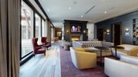 Located at 170 S 6th St in Philadelphia's historic Old City neighborhood, this single-floor amenity space offers a thoughtfully curated collection of social and recreational areas unified by a refined, contemporary design aesthetic. The layout is anchored by a spacious main lounge, where wide-plank hardwood flooring, plush seating arrangements, and a sleek gas fireplace beneath a wall-mounted television create an inviting atmosphere. Generous floor-to-ceiling windows frame views of the surrounding cityscape, including the distinctive red steel truss structure of a neighboring landmark, flooding the interior with natural light.

Steel-framed glass partitions delineate distinct zones throughout the floor, including a dedicated billiards area centered on a handsome red-felt pool table beneath a sculptural brass chandelier. Adjacent dining nooks with warm wood furniture offer intimate gathering spots next to the expansive windows. A fully equipped chef's kitchen features dark granite countertops, stainless steel appliances, a gas cooktop, and open shelving with a decorative tile backsplash, complemented by globe pendant lighting.

A dedicated indoor golf simulator room, complete with artificial turf flooring, a projection screen, and a full set of clubs, rounds out the recreational offerings. Geometric-patterned tile in the entryway corridors and curated artwork throughout add polished finishing touches to this comprehensive amenity floor.