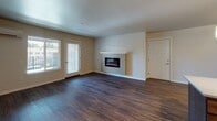 This single-floor residence offers a thoughtfully designed layout that balances functionality and comfort throughout its living spaces. The kitchen is a standout feature, showcasing rich dark wood cabinetry, light-toned countertops, and a full suite of stainless steel appliances including a range, microwave, dishwasher, and refrigerator. A peninsula island provides additional prep space and casual seating, while a pendant light adds a stylish focal point. Wood-look flooring flows throughout the main living areas, lending warmth and visual continuity. The living room is both spacious and inviting, anchored by a wall-mounted electric fireplace with a classic white mantel surround. A glass door provides access to an outdoor area and allows natural light to fill the room. An adjacent dining or flex space connects seamlessly to the kitchen, enhancing the open feel of the main floor. The bedroom is bright and airy, featuring dual windows with views of lush greenery and fitted with plush carpeting for added comfort. The bathroom is clean and practical, offering a full tub and shower combination, wood-look flooring, a vanity with storage, and accessibility-friendly grab bars. Overall, the space presents a move-in ready, modern aesthetic with durable finishes and a functional flow.