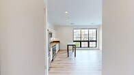 Located in downtown Appleton, Wisconsin, this 2-bedroom, 2-bathroom residence offers a thoughtfully designed, single-floor layout with a clean, modern aesthetic throughout. The open-concept kitchen and living area serves as the heart of the home, featuring light hardwood flooring, recessed lighting, and crisp white cabinetry. The kitchen is equipped with stainless steel appliances — including a refrigerator, electric range, microwave, and dishwasher — paired with a dark countertop for a contemporary contrast. A dining table fits naturally within the space, positioned near expansive black-framed grid windows that flood the area with natural light and offer open views of the surrounding cityscape. Both bedrooms are carpeted and well-lit, each featuring large black-framed windows that frame elevated views of downtown Appleton and the neighboring greenery. The primary bedroom includes a spacious sliding double-door closet. The two bathrooms are finished with neutral tile flooring and white vanities; one features a walk-in shower, while the other includes a bathtub. In-unit stacked laundry is also present. The overall ambiance is bright, clean, and contemporary, well-suited for urban living.