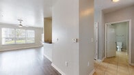 This single-story residence offers a well-organized layout with a neutral color palette and consistent wood-style flooring throughout the main living areas. The open living room is a standout feature, characterized by crown molding, a ceiling fan, and large windows fitted with blinds that allow generous natural light while offering views of the surrounding exterior. Track lighting and additional ceiling fixtures provide ample illumination throughout.

The kitchen is defined by its pass-through bar with dark granite-style countertops, warm-toned wood cabinetry, tile flooring, and stainless steel appliances including an electric range and over-the-range microwave. The pass-through design connects the kitchen to the dining and living area, enhancing the open feel of the shared spaces.

A hallway connects the living zones to the private areas of the unit, with a textured accent wall and thermostat centrally located for convenience. The bedrooms feature wood-style flooring, ceiling fans, and windows that provide natural light. One bedroom includes direct access to the bathroom.

The bathroom is well-appointed with a dual-sink vanity, warm wood cabinetry, dark countertops, a large mirror, tile flooring, and a soaking tub with a tiled surround. The overall ambiance is clean, functional, and move-in ready.