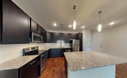Located at 401 Coit Rd in McKinney, Texas, this single-floor residence offers a well-designed layout with consistent, high-quality finishes throughout. The kitchen serves as a standout feature, showcasing dark espresso cabinetry that extends to the ceiling for ample storage, granite countertops, a subway tile backsplash, and a full suite of stainless steel appliances including a refrigerator, range, microwave, and dishwasher. A central island with matching granite provides additional prep space and a natural gathering point. Rich hardwood-style flooring runs throughout the entire unit, lending warmth and visual continuity from room to room. The open living area is bright and spacious, benefiting from natural light through large windows and a sliding glass door, with a ceiling fan adding comfort overhead. The bedrooms are generously proportioned, each with natural light from well-positioned windows and ceiling fans. The bathroom is finished with the same dark cabinetry and granite vanity as the kitchen, offering a cohesive aesthetic, and includes a tiled tub-shower combination. Clean white walls and classic panel doors complete the interior, creating a neutral, move-in-ready environment throughout.