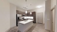 Located at 2610 Erwin Rd in Durham, North Carolina, this single-floor residence offers a clean, modern aesthetic with thoughtfully designed living spaces. The open-concept kitchen serves as a central highlight, showcasing dark espresso-toned cabinetry that contrasts elegantly with bright white countertops and a matching kitchen island with a built-in sink. Stainless steel appliances, including a French door refrigerator with ice maker, electric range, and microwave, add a polished, contemporary feel. Stylish pendant lighting hangs above the island, complemented by a track lighting system overhead, ensuring the space is well-lit and inviting. Light wood-look flooring runs throughout, contributing to the airy, cohesive atmosphere. Tall upper cabinetry provides generous storage, while the overall layout is efficient and functional. A neutral color palette of soft whites and warm grays creates a calm, versatile backdrop suited to a variety of interior styles. The entry door is conveniently situated near the kitchen, contributing to an intuitive flow throughout the single-level floor plan. This space combines modern design sensibilities with practical features, making it a comfortable and stylish place to call home.