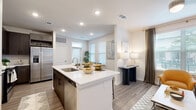 This well-appointed 2-bedroom, 2-bathroom single-story residence features a thoughtfully designed open-concept layout that seamlessly connects the kitchen, dining, and living areas. The kitchen is a standout, showcasing dark wood cabinetry, quartz countertops, a central island with an undermount sink, and a full suite of stainless steel appliances including a side-by-side refrigerator, electric range with microwave, and dishwasher. A white tile backsplash adds a clean, modern touch. The adjacent dining area benefits from a wall of windows fitted with horizontal blinds, filling the space with natural light, while the living room offers a comfortable, airy atmosphere with additional window access and wood-look plank flooring found throughout the unit. The primary bedroom is a well-sized retreat with large windows overlooking a green outdoor area, providing both light and outdoor views. Each bedroom is served by its own dedicated bathroom, with dark vanity cabinetry, white quartz counters, and a tub-shower combination. Both bedrooms include closets, with the primary featuring a spacious walk-in closet with wrap-around shelving and hanging rods. Recessed lighting, neutral wall tones, and consistent wood-look flooring create a cohesive, modern aesthetic throughout.