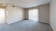 Located at 9300 Orchard Blvd in Midwest City, Oklahoma, this 2-bedroom, 1-bathroom single-floor unit offers a practical and comfortable layout. The open combined living, dining, and kitchen area forms the heart of the home, with plush gray carpet, a textured ceiling, and a ceiling fan adding to the welcoming atmosphere. A large sliding glass door fitted with vertical blinds floods the living space with natural light and provides outdoor views. The kitchen is equipped with a white range and ample cabinetry. The primary bedroom is a well-proportioned retreat featuring a ceiling fan with light fixture, natural light from a window, and soft carpet underfoot. The second bedroom also enjoys natural light through its own window and comfortable carpeting. Both bedrooms are served by a total of three closets, offering generous storage. The shared bathroom includes a full tub-shower combo with clean white surrounds and wood-look flooring. A dedicated utility room adds further practicality. Neutral gray walls, white trim, and consistent finishes throughout create a cohesive and move-in ready environment throughout this Midwest City residence.