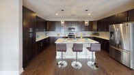 This single-floor residence presents a thoughtfully designed interior characterized by dark hardwood flooring, neutral warm-toned walls, and an open, flowing layout. The gourmet kitchen serves as a central highlight, featuring rich espresso cabinetry extending to the ceiling, light quartz countertops, a mosaic tile backsplash, stainless steel appliances, and a large central island with seating for multiple guests. Pendant lighting adds a polished finishing touch overhead.

The dining area benefits from multiple windows framing elevated city views, complemented by roller shades for adjustable light control. The living area is intimate yet well-proportioned, with a wall-mounted media unit and access to natural light through city-facing windows.

Both bedrooms are generously sized, each featuring multiple windows that capture sweeping urban vistas, dark hardwood flooring, and plush area rugs adding warmth. The primary bedroom offers ample space for a full furniture arrangement with a sitting area.

The bathrooms are finished with large-format neutral floor tiles, glass-enclosed walk-in showers with mosaic tile accent strips, recessed lighting, and clean white fixtures, delivering a spa-like atmosphere throughout.