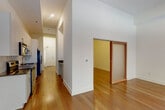 This single-floor residence showcases a clean, contemporary design throughout. The open-concept living area is bright and spacious, with warm hardwood flooring that extends seamlessly through the main living spaces. Large black-framed sliding glass doors lead to a private balcony, flooding the room with natural light and offering views of the surrounding neighborhood. An additional window further enhances the airy atmosphere.

The kitchen is efficiently designed along a galley-style corridor and features light wood cabinetry with brushed nickel hardware, dark granite countertops, a stainless steel under-mount sink, and a geometric hexagonal tile backsplash. Stainless steel appliances, including an electric range, over-the-range microwave, and refrigerator, complete the kitchen.

A hallway connects the living areas to the bedroom, which boasts impressively tall ceilings, a double-door closet, and continued hardwood flooring. A sliding barn-style door provides access to an additional room. The bathroom is finished with a granite-topped vanity, light wood cabinetry, brushed nickel fixtures, and a glass-enclosed shower. Recessed lighting throughout maintains a polished, modern ambiance.