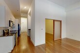 This single-floor residence showcases a clean, contemporary design throughout. The open-concept living area is bright and spacious, with warm hardwood flooring that extends seamlessly through the main living spaces. Large black-framed sliding glass doors lead to a private balcony, flooding the room with natural light and offering views of the surrounding neighborhood. An additional window further enhances the airy atmosphere.

The kitchen is efficiently designed along a galley-style corridor and features light wood cabinetry with brushed nickel hardware, dark granite countertops, a stainless steel under-mount sink, and a geometric hexagonal tile backsplash. Stainless steel appliances, including an electric range, over-the-range microwave, and refrigerator, complete the kitchen.

A hallway connects the living areas to the bedroom, which boasts impressively tall ceilings, a double-door closet, and continued hardwood flooring. A sliding barn-style door provides access to an additional room. The bathroom is finished with a granite-topped vanity, light wood cabinetry, brushed nickel fixtures, and a glass-enclosed shower. Recessed lighting throughout maintains a polished, modern ambiance.
