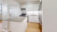 This efficiently laid-out 1-bedroom, 1-bathroom unit offers a clean, modern aesthetic throughout its single floor. Light hardwood flooring runs continuously across all rooms, creating a cohesive and warm feel. The spacious living room is a standout feature, boasting expansive floor-to-ceiling windows that flood the space with natural light and offer sweeping views of the surrounding cityscape. A baseboard heating system runs along the window wall, ensuring year-round comfort. The kitchen is thoughtfully designed with sleek white cabinetry extending to the ceiling, a stainless steel stove, stainless steel refrigerator, an integrated range hood, and a functional center island with a neutral countertop — ideal for meal preparation. The bedroom is a well-proportioned retreat, featuring a large sliding-door closet, a bright window with outdoor views, and the same consistent hardwood flooring. The bathroom is finished in a clean, all-white palette with full-wall tile surrounding a soaking bathtub and shower combination. Neutral grey walls throughout the unit contribute to a calm, understated ambiance, making this a versatile and move-in-ready space.