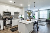 Located at 1000 Everly Way in Gainesville, Georgia, this single-floor residence offers a thoughtfully designed open-concept layout filled with modern finishes and natural light. The kitchen is a standout feature, boasting crisp white shaker cabinetry, granite countertops, a large center island with seating, a grey subway tile backsplash, and a full suite of stainless steel appliances. Warm hardwood-style flooring flows throughout the main living areas, connecting the kitchen seamlessly to the living room. The living area is bright and inviting, with large windows that allow generous natural light, a ceiling fan, and access to an outdoor balcony. The bedroom features a distinctive shiplap accent wall, large windows with sheer drapes, and soft carpet underfoot, creating a cozy and restful retreat. A second bedroom offers a clean, airy aesthetic with ample natural light and neutral tones. The bathroom is finished with granite-topped white vanity cabinetry, hardwood-style flooring, and direct access to a well-organized walk-in closet. Throughout the space, the design strikes a balance between modern functionality and warm, comfortable living.