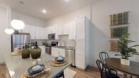 This single-floor residence is thoughtfully designed with a clean, contemporary aesthetic throughout. The kitchen serves as a functional centerpiece, outfitted with crisp white shaker cabinetry extending to the ceiling for generous storage, grey quartz-style countertops, a tile backsplash, and a full suite of stainless steel appliances including a refrigerator, range, over-the-range microwave, and dishwasher. Wood-look plank flooring runs through the kitchen and flows into the adjoining dining and living areas, creating visual continuity. The living room is bright and welcoming, featuring a ceiling fan, neutral walls, and a glass-paned door that opens to an outdoor patio, allowing natural light to fill the space. The bedroom is carpeted for comfort, equipped with a ceiling fan, a window with outdoor views, and ample wall space. The bathroom features a white vanity with undermount sink, a tub-shower combination with tile surround, and wood-look flooring. Throughout the unit, a neutral color palette and recessed lighting contribute to a clean, modern ambiance.