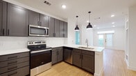 Located on Nash Hernandez Sr Road in Austin, TX, this single-floor residence showcases a contemporary design with clean lines and a neutral color palette throughout. The open-concept kitchen is a standout feature, equipped with stainless steel appliances including a range, microwave, dishwasher, and refrigerator. Dark gray shaker-style cabinetry is paired with crisp white quartz countertops and a classic white subway tile backsplash. A peninsula with a built-in sink and pendant lighting overhead adds both functionality and a modern aesthetic. Light bamboo-style flooring runs throughout the main living and kitchen areas, complementing the bright, recessed lighting above.

The bathroom continues the cohesive design theme with a dual-sink vanity topped with white quartz counters, dark cabinetry with black hardware, a large framed mirror, open shelving, and a full soaking tub. Light flooring and white walls keep the space feeling fresh and clean.

The bedroom features soft carpeting, built-in wall shelving, and ample space. Natural light filters in through windows visible from the main living area. The overall ambiance is modern, clean, and move-in ready.