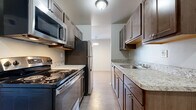 This single-floor, two-bedroom, one-bathroom residence in Birmingham, Michigan offers a practical and comfortable layout with a clean, neutral aesthetic throughout. The galley-style kitchen is a functional highlight, featuring dark wood cabinetry with brushed nickel hardware, light granite-style countertops, stainless steel appliances including a refrigerator, range, and built-in microwave, and a stainless steel sink. Light wood-look flooring runs through the kitchen and connecting hallway, providing a smooth transition between spaces.

Both bedrooms are generously proportioned, carpeted, and filled with natural light through sizable windows with blinds. The primary bedroom benefits from two windows positioned on adjacent walls, allowing sunlight from multiple directions. Each bedroom includes closet space, with at least one featuring a walk-in closet. The living area is equally well-lit, with a large window and plush carpeting underfoot.

The bathroom is finished with large-format tile flooring, a dark wood vanity with granite-style countertops, and a glass-enclosed shower with tile surround. The overall palette of neutral tones and consistent finishes creates a cohesive, move-in-ready environment throughout the unit.