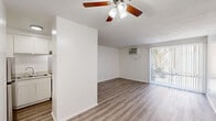 Located at 3301 Yorba Linda Blvd in Fullerton, CA, this single-floor unit offers a clean, functional layout with a bright, neutral aesthetic throughout. The open-concept living and kitchen area forms the heart of the space, featuring light wood-look flooring that extends seamlessly across the entire unit. The living area is outfitted with a ceiling fan with lighting, a wall-mounted air conditioning unit, and a full-length sliding glass door dressed with vertical blinds, allowing natural light to filter in while providing outdoor access and views of the surrounding greenery. An additional window with blinds further contributes to the unit's airy feel. The kitchen is efficiently designed with white cabinetry, granite-look countertops, a stainless steel refrigerator, a stainless range hood, and a double-basin sink — all connected to the living space via a half-wall breakfast bar, creating an open and social flow. Two bathrooms serve the unit; one features a long vanity with an integrated sink, a framed mirror, and access to a separate tub/shower room, while the second is a straightforward tub/shower combo with white surround. Throughout, the clean white walls and consistent flooring create a cohesive and well-maintained living environment.