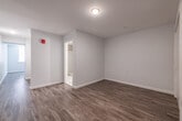 This single-floor unit offers a clean, modern design with a thoughtfully arranged open layout. The living area is bright and spacious, featuring warm hardwood-style flooring and neutral gray walls that create a versatile backdrop. Large windows allow natural light to fill the space, enhancing its open and airy feel.

The kitchen is efficiently designed and fully equipped with stainless steel appliances, including a range with oven, dishwasher, refrigerator, and microwave. Sleek gray cabinetry with contemporary hardware lines the walls, complemented by light countertops and a single-basin sink — offering both functionality and a modern aesthetic.

The bathroom is finished with large-format tile flooring, a dark-toned vanity with an undermount sink, a well-lit mirror, and a louvered closet door, providing practical storage. The layout also includes a dedicated closet or utility area, visible in the floor plan, which adds to the unit's organizational convenience.

Throughout the space, clean white trim and baseboards contrast neatly with the flooring, and a fire safety device is prominently mounted on the wall, underscoring attention to safety standards. The overall design is modern, functional, and move-in ready, making it a practical and attractive living space.