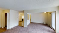 Located at 600 South Dayton Street in Denver, Colorado, this single-floor residence offers a straightforward and functional layout designed for comfortable everyday living. The main living area is finished with plush wall-to-wall carpeting in a neutral tone, creating a warm and inviting atmosphere. White walls throughout keep the space feeling bright and clean, while a textured popcorn ceiling adds a classic touch overhead. A baseboard heating unit along the wall ensures efficient climate control throughout the cooler months. The living area flows naturally toward an adjacent dining and kitchen space, where hardwood-style flooring provides a visual transition between zones. The kitchen is equipped with standard appliances, including a refrigerator and range, and is accented by a chandelier overhead that adds a subtle decorative element to the dining area. A partial wall divider thoughtfully separates the living space from the kitchen corridor, maintaining an open feel while providing a sense of structure. Additional rooms are accessible through interior doorways, including what appears to be a hallway leading to further living quarters. The overall ambiance is clean, neutral, and move-in ready, making this Denver residence a practical and welcoming home.