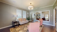 This single-floor space is thoughtfully designed with a cohesive neutral color palette, crown molding, and warm hardwood and carpet flooring that carry throughout. The front sitting area makes a refined first impression, featuring a drum pendant chandelier, textured ceiling, and ample natural light from multiple windows with white plantation blinds. Framed artwork and a large mirror add depth and elegance to the room, while an adjacent private office provides a quiet, professional retreat with its own seating.

The main living area is generously sized with vaulted ceilings, large windows overlooking the outdoors, and a brick fireplace with a rustic wood mantle as a standout focal point. Rich leather seating and a wall-mounted television make this an inviting and functional gathering space.

The dining room connects seamlessly to the outdoors through a set of French doors flanked by wide windows, flooding the room with natural light and offering pleasant outdoor views. A substantial dark wood dining table with upholstered chairs anchors the space comfortably.

The kitchenette is well-equipped with warm honey-toned cabinetry, granite countertops, a classic white subway tile backsplash, and stainless steel appliances, providing practical amenities within the overall layout.