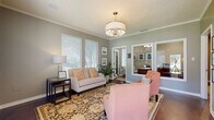 This single-floor space is thoughtfully designed with a cohesive neutral color palette, crown molding, and warm hardwood and carpet flooring that carry throughout. The front sitting area makes a refined first impression, featuring a drum pendant chandelier, textured ceiling, and ample natural light from multiple windows with white plantation blinds. Framed artwork and a large mirror add depth and elegance to the room, while an adjacent private office provides a quiet, professional retreat with its own seating.

The main living area is generously sized with vaulted ceilings, large windows overlooking the outdoors, and a brick fireplace with a rustic wood mantle as a standout focal point. Rich leather seating and a wall-mounted television make this an inviting and functional gathering space.

The dining room connects seamlessly to the outdoors through a set of French doors flanked by wide windows, flooding the room with natural light and offering pleasant outdoor views. A substantial dark wood dining table with upholstered chairs anchors the space comfortably.

The kitchenette is well-equipped with warm honey-toned cabinetry, granite countertops, a classic white subway tile backsplash, and stainless steel appliances, providing practical amenities within the overall layout.