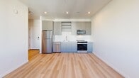 Located at 1390 NE Compton Dr in Hillsboro, Oregon, this thoughtfully designed one-bedroom, one-bathroom unit offers a clean, contemporary aesthetic throughout its single-floor layout. The open-concept living, dining, and kitchen area serves as the heart of the home, featuring light wood-tone flooring that flows seamlessly from room to room. The modern kitchen is equipped with stainless steel appliances — including a refrigerator, range, microwave, and dishwasher — complemented by sleek gray cabinetry, open shelving, and a classic white subway tile backsplash. Recessed lighting illuminates the space efficiently. The bedroom is a calm, well-proportioned retreat with bright white walls, the same warm wood flooring, and a large window that invites natural light and views of the surrounding contemporary neighborhood. Two closets provide generous storage, with wire shelving systems already in place. The bathroom features a full soaking tub with tiled surround and a gray vanity, while also accommodating in-unit laundry. Clean lines, neutral tones, and a well-considered layout make this a highly functional and modern living space.