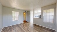 This single-floor, 1-bedroom, 1-bathroom unit is thoughtfully designed to maximize its compact footprint. The entry hallway, finished with wood-style flooring, provides a welcoming transition into the open living area. The living room is bright and airy, featuring multiple windows with horizontal blinds that allow ample natural light to fill the space. The wood-style flooring continues throughout, complemented by neutral gray walls and a textured ceiling. A half-wall pass-through connects the living room to the kitchen, which is a standout feature of the unit. The kitchen is outfitted with white cabinetry, white countertops, stainless steel appliances including a dishwasher, range, and microwave, and a striking blue mosaic tile backsplash that adds a pop of color. The bedroom is generously sized and features plush carpet flooring, a window for natural light, and direct access to a walk-in closet with built-in shelving and hanging rods. The bathroom includes a full tub-shower combo with white tile surround and clean, simple fixtures. Overall, the unit presents a clean, modern aesthetic throughout with consistent finishes and a practical, well-organized layout.