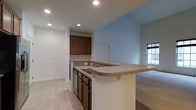 Located at 12001 Old Vine Blvd in Lewes, Delaware, this two-story home offers a well-designed layout that balances functionality and comfort. The kitchen serves as a central highlight, featuring rich dark wood cabinetry that provides ample storage, a tile countertop peninsula with a breakfast bar overhang ideal for casual dining or entertaining, and a built-in sink with dishwasher. Recessed lighting illuminates the space from above, complementing the light tile flooring that runs throughout the kitchen area. The soft blue accent wall adds a touch of color and warmth to the open-concept design. The kitchen flows naturally into the adjoining living area, which transitions to plush carpeting and is brightened by a window that invites natural light. The open sightlines between spaces create a cohesive and spacious feel throughout the main level. The two-story layout provides additional living space above, offering flexibility for bedrooms or additional functional areas. Overall, the home presents a clean, move-in-ready environment with a neutral palette that accommodates a variety of interior styles.