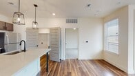 This single-floor space is designed with a contemporary aesthetic and a practical open-concept layout. The kitchen serves as a central highlight, featuring dark espresso-toned shaker cabinetry, a full suite of stainless steel appliances including an electric range, built-in microwave, and refrigerator, complemented by a white quartz countertop and a marbled subway tile backsplash. A central island with seating and three industrial-style cage pendant lights anchors the space, making it ideal for both cooking and casual dining. Rich hardwood-style flooring extends throughout the main living areas, adding warmth and visual continuity.

The bedrooms are carpeted for comfort and feature neutral walls, natural light from blinds-fitted windows, and ceiling fans. A walk-in closet with built-in shelving and hanging rods provides ample storage. The bathrooms are finished with consistent dark cabinetry, quartz countertops, and wood-look flooring. The primary bathroom offers a double-sink vanity with framed mirror and stylish matte black fixtures, while a secondary bathroom includes a soaking tub with tiled surround. The overall palette of crisp whites and warm wood tones creates a clean, modern ambiance throughout.