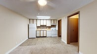 This single-floor unit offers a practical and functional layout designed for comfortable everyday living. The open-plan living and kitchen area forms the heart of the space, where light wood-look flooring transitions seamlessly into plush carpeting in the living zone. The kitchen is equipped with white cabinetry accented by wood-tone trim, a mosaic tile backsplash, a full suite of white appliances including a refrigerator, electric range, and dishwasher, as well as a skylight that draws in natural light. A ceiling fan overhead serves both the kitchen and living area. The living space is generously proportioned, offering an open and airy feel with neutral beige walls and clean white baseboards throughout. The bedroom is carpeted and features a ceiling fan with light, a window dressed with blinds that allows natural light to filter in, and a textured ceiling. The full bathroom includes a single-sink vanity with a marble-look countertop, a tub-shower combination, and wood-look flooring. A dedicated laundry room houses a full-sized washer and dryer alongside a utility sink and water heater, providing added convenience. The overall ambiance is clean, neutral, and move-in ready.