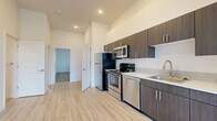 This well-appointed 2-bedroom, 2-bathroom unit offers a thoughtfully designed layout across a single floor. The open-concept living and kitchen area creates a spacious, airy feel, anchored by light wood-style luxury vinyl flooring and crisp white walls brightened by recessed lighting. The kitchen is a standout feature, outfitted with a full suite of stainless steel appliances — including a refrigerator, electric range, over-the-range microwave, and dishwasher — complemented by dark espresso-toned cabinetry, white quartz-style countertops, and a classic subway tile backsplash. A single-basin sink with a modern gooseneck faucet adds a refined touch. The living area is generously proportioned, with windows fitted with blinds that allow for natural light control. Both bedrooms are carpeted for comfort and each features a sliding-door closet with built-in shelving. The primary bedroom is notably spacious with tall ceilings and large windows. Each bathroom is clean and functional, featuring a full soaking tub and shower combination in an all-white surround. The unit's neutral palette, modern finishes, and practical layout make it a versatile and move-in-ready space.