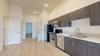This well-appointed 2-bedroom, 2-bathroom unit offers a thoughtfully designed layout across a single floor. The open-concept living and kitchen area creates a spacious, airy feel, anchored by light wood-style luxury vinyl flooring and crisp white walls brightened by recessed lighting. The kitchen is a standout feature, outfitted with a full suite of stainless steel appliances — including a refrigerator, electric range, over-the-range microwave, and dishwasher — complemented by dark espresso-toned cabinetry, white quartz-style countertops, and a classic subway tile backsplash. A single-basin sink with a modern gooseneck faucet adds a refined touch. The living area is generously proportioned, with windows fitted with blinds that allow for natural light control. Both bedrooms are carpeted for comfort and each features a sliding-door closet with built-in shelving. The primary bedroom is notably spacious with tall ceilings and large windows. Each bathroom is clean and functional, featuring a full soaking tub and shower combination in an all-white surround. The unit's neutral palette, modern finishes, and practical layout make it a versatile and move-in-ready space.