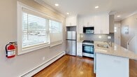 Located at 1 Kowal St, Unit A1, in Clifton, NJ, this efficiently designed single-floor unit offers a thoughtfully organized layout that maximizes every square foot. Rich hardwood flooring flows throughout the space, complemented by crown molding and recessed lighting that lend a polished, finished look to every room.

The open-concept living and kitchen area forms the heart of the unit. The kitchen is outfitted with crisp white shaker cabinetry, granite countertops, a subway tile backsplash, and stainless steel appliances including a gas range, refrigerator, and built-in microwave. A central island with a single-basin sink provides additional prep space and casual seating. Natural light fills the living area through multiple windows fitted with blinds, creating a bright and welcoming atmosphere.

A stylish sliding barn door provides access to the in-unit laundry area, which houses a stacked washer and dryer — a convenient and space-conscious feature. The hallway connects to a well-appointed bathroom featuring a glass-enclosed shower with clean white tile surround and mosaic accent detailing, along with a window for natural ventilation. A dedicated closet offers additional storage. The unit also includes its own private entrance with a classic panel door, adding to the sense of independence and functionality.