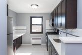 Located at 398 Church St in Hasbrouck Heights, NJ, this single-floor unit offers a well-organized layout with a clean, modern aesthetic throughout. The living area is immediately welcoming, featuring warm honey-toned hardwood floors that reflect natural light streaming in through the windows. Cool-toned grey walls provide a calm, neutral backdrop, while recessed lighting and a radiator unit ensure year-round comfort.

The kitchen is thoughtfully outfitted with rich dark cabinetry paired with light quartz countertops, creating a striking contrast. Stainless steel appliances — including a gas range and over-the-range microwave — add a contemporary touch, while a classic white subway tile backsplash ties the design together. A window above the counter brings in additional natural light and views of the surrounding neighborhood.

The bedroom continues the hardwood flooring and grey wall palette, offering a bright and serene atmosphere with its own window and radiator. The bathroom is neatly finished with wood-look tile flooring, white fixtures, and a window for natural ventilation. The overall layout is efficient and well-connected, making the most of every square foot while maintaining a comfortable, cohesive living environment throughout.