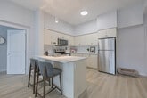Located at 70 Dean Avenue in Barrie, Ontario, this well-appointed two-bedroom, two-bathroom single-floor residence offers a bright, modern living experience. The open-concept layout seamlessly connects the kitchen and living room, creating a generous and functional shared space. The kitchen is fitted with crisp white cabinetry, a central island with a built-in sink and dishwasher, stainless steel appliances including a full-size refrigerator and range, and pendant lighting — all set atop light-toned hardwood flooring that runs throughout the home. The living room enjoys an abundance of natural light through large sliding glass doors that open to an outdoor balcony, offering views of the surrounding neighbourhood. The spacious primary bedroom features a tray ceiling, wide windows with outdoor views, and a dedicated walk-in closet with wire shelving and hanging storage. The second bedroom is well-proportioned with a large window and the same warm hardwood flooring. Both bathrooms are finished in a clean, neutral palette, each featuring a full soaker tub-shower combination and marble-style tile flooring. A hallway, utility room, and additional closet space complete the thoughtfully designed layout, providing practical storage throughout.