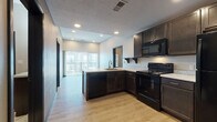 Located on E Cherry Street in Springfield, Missouri, this single-story unit presents a thoughtfully designed interior with a contemporary aesthetic carried throughout. The open-concept kitchen serves as a central feature, outfitted with dark espresso cabinetry, light marble-patterned countertops, and a full suite of black appliances including an electric range, over-the-range microwave, dishwasher, and refrigerator. A peninsula with an undermount sink provides additional workspace and naturally connects the kitchen to the living area, which benefits from access to a private balcony through sliding glass doors, allowing natural light to filter into the space. Light wood-style laminate flooring runs through the main living and kitchen areas, offering a warm contrast to the bold cabinetry. The bedrooms feature neutral carpet and windows that bring in natural light, while dark-framed doors add a consistent modern touch throughout. Each bedroom provides access to a closet for dedicated storage. The bathrooms are finished with large-format marble-look tile flooring, dark vanity cabinetry with light countertops, and a shower-tub combination, creating a clean and polished look. The textured ceiling and recessed lighting complete the unit's modern, functional design.