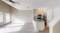 This well-appointed two-story residence offers a thoughtfully designed layout with clean, modern finishes throughout. The main level welcomes you with an entryway featuring a white brick fireplace and a carpeted staircase with a warm wood handrail leading to the upper floor. Light-toned hardwood-style flooring flows consistently throughout both levels, creating a cohesive and airy feel.

The open-concept living area is anchored by impressively vaulted ceilings and a ceiling fan, while a bank of large windows along one wall floods the space with abundant natural light. The seamless transition into the kitchen makes this an ideal space for entertaining. The kitchen is well-equipped with stainless steel appliances, including a refrigerator, range, and built-in microwave, complemented by white shaker-style cabinetry, a classic subway tile backsplash, and a peninsula with a dark stone countertop and an integrated sink.

The upper level includes additional rooms with tall ceilings and generous proportions. The bathroom features a modern floating vanity with a clean white basin, a brushed nickel towel ring, and a full tub-shower combination. Throughout, neutral wall tones and abundant natural light contribute to a bright, open, and contemporary atmosphere.