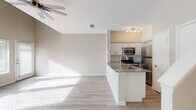 This well-appointed two-story residence offers a thoughtfully designed layout with clean, modern finishes throughout. The main level welcomes you with an entryway featuring a white brick fireplace and a carpeted staircase with a warm wood handrail leading to the upper floor. Light-toned hardwood-style flooring flows consistently throughout both levels, creating a cohesive and airy feel.

The open-concept living area is anchored by impressively vaulted ceilings and a ceiling fan, while a bank of large windows along one wall floods the space with abundant natural light. The seamless transition into the kitchen makes this an ideal space for entertaining. The kitchen is well-equipped with stainless steel appliances, including a refrigerator, range, and built-in microwave, complemented by white shaker-style cabinetry, a classic subway tile backsplash, and a peninsula with a dark stone countertop and an integrated sink.

The upper level includes additional rooms with tall ceilings and generous proportions. The bathroom features a modern floating vanity with a clean white basin, a brushed nickel towel ring, and a full tub-shower combination. Throughout, neutral wall tones and abundant natural light contribute to a bright, open, and contemporary atmosphere.