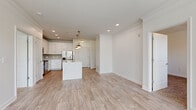 Located at 2103 Defoors Ferry Rd NW in Atlanta, Georgia, this single-floor residence offers a clean, modern aesthetic throughout. The open-concept layout connects the kitchen and living areas seamlessly, with light wood-style flooring extending across the main living spaces. The kitchen is a standout feature, showcasing white shaker cabinetry, a subway tile backsplash, stainless steel appliances including a range, microwave, and refrigerator, and a large center island with a white quartz countertop, undermount sink, and stylish brass pendant lighting overhead. Crown molding adds a refined touch to the living area, which also features in-wall speakers and a ceiling fan. Bedrooms are finished with plush carpeting and receive natural light through blinded windows with views of greenery. A dedicated room with glass-paneled exterior door access brings in additional light. The bathroom is well-appointed with white cabinetry, quartz countertops, and a tiled tub-shower combination. A spacious walk-in closet with wire shelving systems provides generous storage. Throughout, a neutral white and warm gray palette creates a bright, cohesive, and inviting atmosphere.
